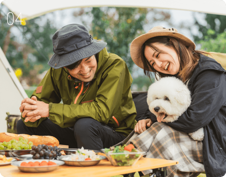 キャンプで食事を楽しむ男女と白い犬